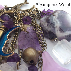 Pu&ograve; includere: Una collana con ciondoli a tema steampunk con una variet&agrave; di ciondoli, tra cui una chiave, una mezzaluna, una pietra di ametista a forma di cuore e un cristallo trasparente. I ciondoli sono attaccati a una catena con una variet&agrave; di perline e altri elementi decorativi.