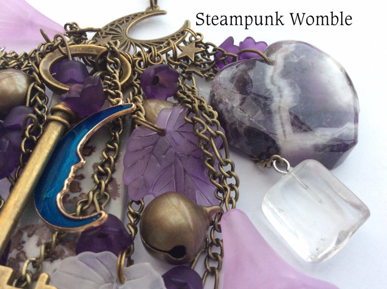 Pu&ograve; includere: Una collana con ciondoli a tema steampunk con una variet&agrave; di ciondoli, tra cui una chiave, una mezzaluna, una pietra di ametista a forma di cuore e un cristallo trasparente. I ciondoli sono attaccati a una catena con una variet&agrave; di perline e altri elementi decorativi.