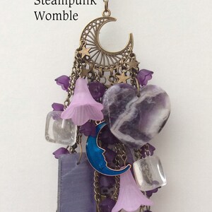 Pu&ograve; includere: Un ciondolo in stile steampunk viola e oro con una luna crescente, stelle, campane e cristalli di ametista. Il ciondolo &egrave; etichettato "Steampunk Womble".