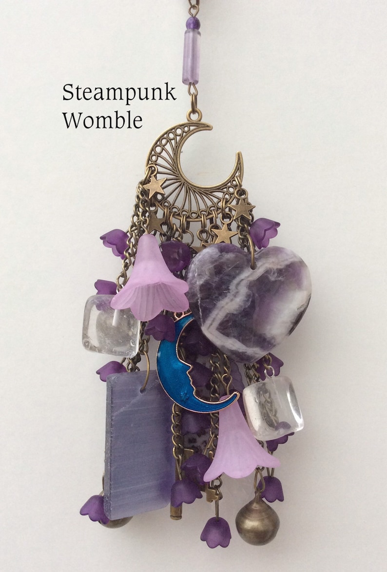 Pu&ograve; includere: Un ciondolo in stile steampunk viola e oro con una luna crescente, stelle, campane e cristalli di ametista. Il ciondolo &egrave; etichettato "Steampunk Womble".