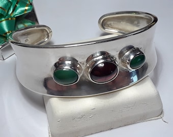 May include: A silver cuff bracelet with three cabochon gemstones. The gemstones are green, purple, and green. The bracelet is marked "925" on the inside.