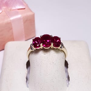 May include: A gold ring with three red ruby stones and small diamonds on the band.