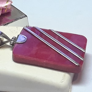 May include: A rectangular pendant with a silver bail and three silver stripes on a deep red background.