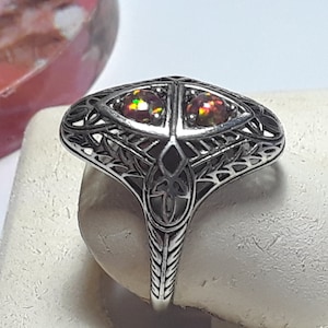May include: A silver filigree ring with two iridescent opal gemstones. The ring has a delicate, intricate design and is set on a white background.