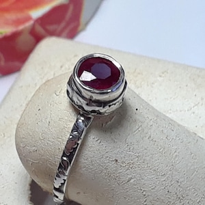 May include: A silver ring with a deep red gemstone set in a textured band.