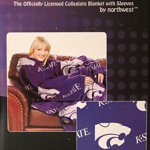 May include: Purple fleece blanket with sleeves featuring the Kansas State Wildcats logo and "K-State" text. The blanket is shown on a person sitting on a couch. The product packaging includes the text "Comfy Throw The Officially Licensed Collegiate Blanket with Sleeves by northwest&trade;&trade;".