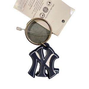 May include: A blue and white New York Yankees logo keychain with a silver key ring. The keychain is officially licensed by Major League Baseball.