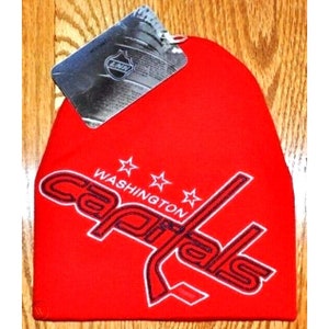 May include: Red knit beanie with a white embroidered Washington Capitals logo. The logo features the team name in a stylized font with three white stars above it.
