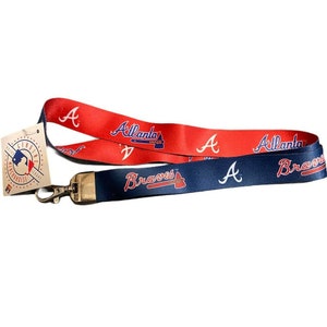 May include: A red and blue lanyard with the Atlanta Braves logo and the words "Atlanta Braves" printed on it. The lanyard has a gold metal clasp.