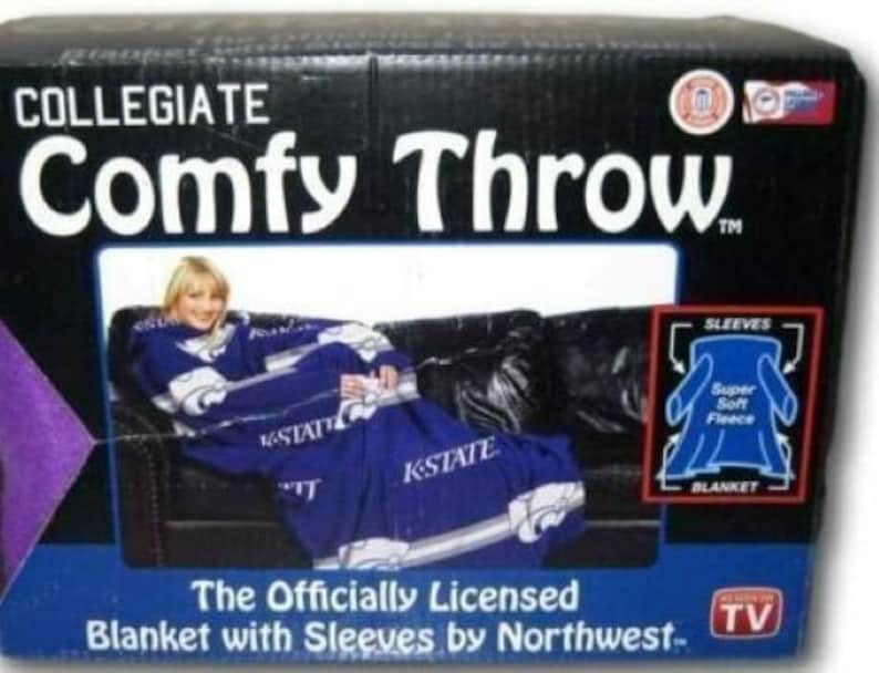 May include: A purple and blue collegiate blanket with sleeves. The blanket features the text "K-State" and a logo. The packaging shows a person wearing the blanket on a couch. The text on the packaging reads "Collegiate Comfy Throw The Officially Licensed Blanket with Sleeves by Northwest... TV"