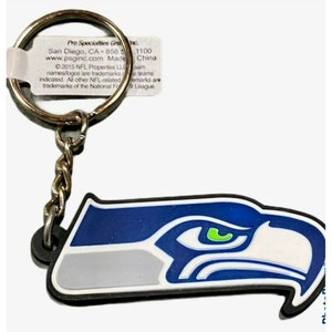 May include: A blue, white, and green Seattle Seahawks logo keychain. The logo is a stylized bird's head with a green eye. The keychain is made of rubber and has a silver metal ring.