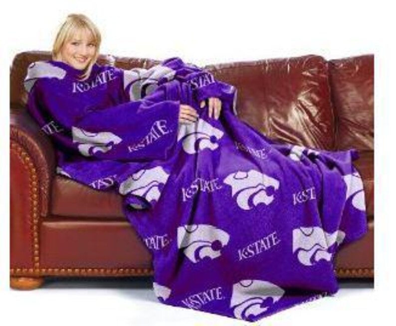 May include: Purple fleece blanket with a large white K-State Wildcat logo and the words "K-State" repeated throughout. The blanket has sleeves and is designed to be worn like a robe.