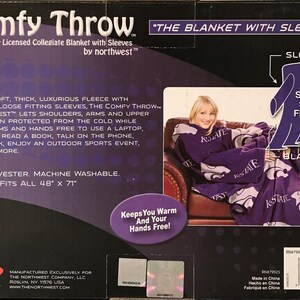May include: Purple fleece blanket with sleeves featuring the text "K-State" and a purple Wildcat logo. The blanket is shown draped over a chair with a person wearing the blanket. The text "Comfy Throw" and "The Blanket with Sleeves" is on the packaging. The packaging also states "Made of soft, thick, luxurious fleece with oversized loose fitting sleeves, the Comfy Throw by Northwest lets shoulders, arms and upper body remain protected from the cold while leaving arms and hands free to use a laptop, TV remote, read a book, talk on the phone, eat a snack, enjoy an outdoor sports event, and much more. 100% Polyester. Machine Washable. One size fits all 48" x 71"."