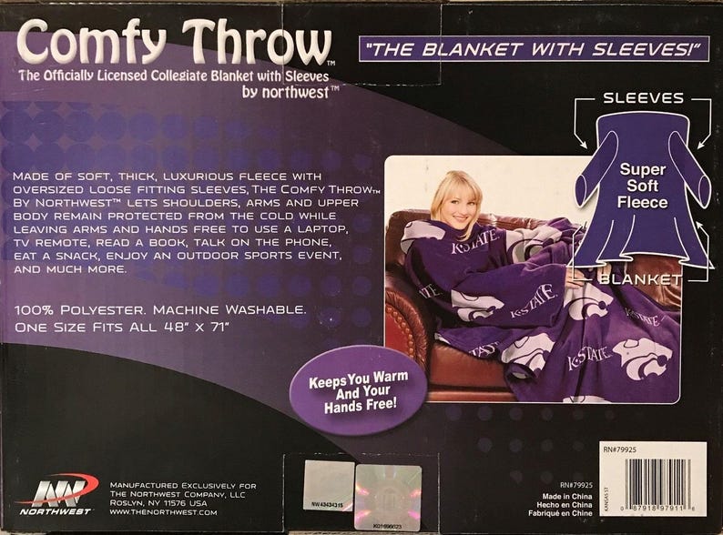 May include: Purple fleece blanket with sleeves featuring the text "K-State" and a purple Wildcat logo. The blanket is shown draped over a chair with a person wearing the blanket. The text "Comfy Throw" and "The Blanket with Sleeves" is on the packaging. The packaging also states "Made of soft, thick, luxurious fleece with oversized loose fitting sleeves, the Comfy Throw by Northwest lets shoulders, arms and upper body remain protected from the cold while leaving arms and hands free to use a laptop, TV remote, read a book, talk on the phone, eat a snack, enjoy an outdoor sports event, and much more. 100% Polyester. Machine Washable. One size fits all 48" x 71"."