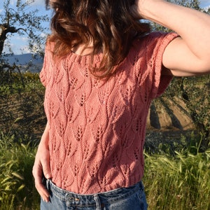 Puede incluir: Una blusa de punto rosa con un patrón de hojas. La blusa tiene mangas cortas y un escote redondo.