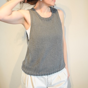 May include: A gray sleeveless knitted top with a round neckline. The top is made of a soft, textured yarn and has a relaxed fit.