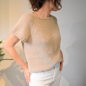 May include: A beige short-sleeved knitted sweater with a round neckline.