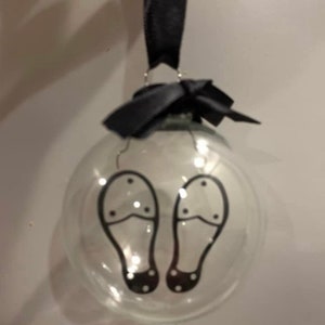 May include: A clear glass ornament with a black ribbon and a black and white illustration of a pair of shoes inside.