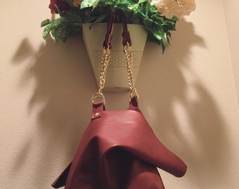 May include: A burgundy leather handbag with gold chain straps hanging from a white planter with a floral arrangement of red, white, and yellow flowers.
