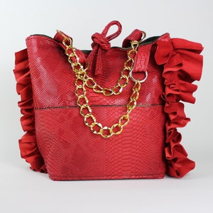 Puede incluir: Bolso rojo con estampado de piel de serpiente y correas de cadena dorada. El bolso tiene un ribete con volantes alrededor de los bordes.
