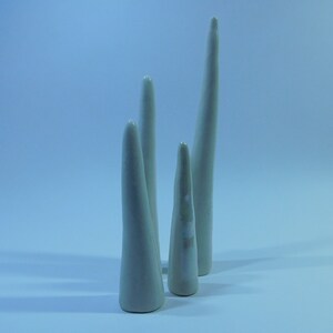 May include: Five white ceramic sculptures in the shape of tall, thin cones. The sculptures are arranged in a row on a light blue surface.