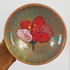 May include: A ceramic bowl with a green and gold striped design and a hand-painted red flower with yellow centers. The bowl is signed "ViolenHeeK".