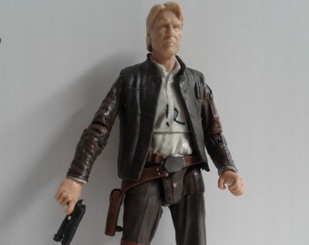 May include: A brown leather jacket with a tan shirt and brown pants. The figure is holding a black blaster in its right hand. The figure is wearing brown boots.