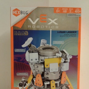 May include: A Hexbug Vex Robotics Lunar Lander Explorer construction kit with 400+ pieces. The kit features a gray and yellow lunar lander with a satellite dish, landing gear, and a radar antenna. The box also includes a small astronaut figure. The box is orange and white with the words "Build Genius" and "STEM Starter" on it.