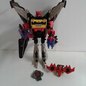May include: A black, red and yellow Transformers action figure with wings, a sword and a gun. The figure is in robot mode and has a detailed design. The figure is standing on a white surface.