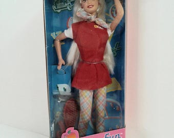 May include: A Special Edition Schooltime Fun Barbie doll with long blonde hair, wearing a red dress over a white shirt, a plaid scarf, and plaid leggings. The doll is inside a pink and blue box featuring school-themed graphics and the text Barbie.