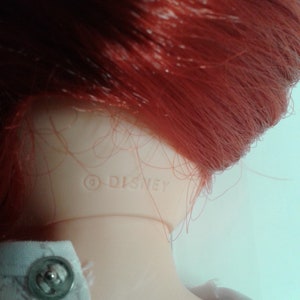 K&ouml;nnte beinhalten: Nahaufnahme des Nackens einer rothaarigen Puppe mit dem Copyright-Symbol und dem Wort "DISNEY", das auf den Kunststoff gedruckt ist.