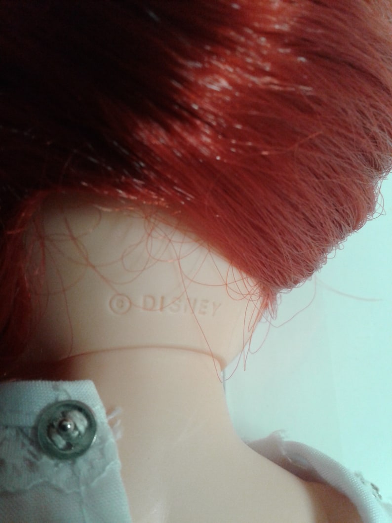 K&ouml;nnte beinhalten: Nahaufnahme des Nackens einer rothaarigen Puppe mit dem Copyright-Symbol und dem Wort "DISNEY", das auf den Kunststoff gedruckt ist.