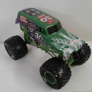 May include: A green and white Grave Digger monster truck toy with large black tyres. The truck features the number "30" and the words "Grave Digger" and "30 Years" on the body. The tyres are marked with "BKT".