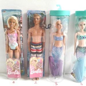 May include: Four Barbie dolls in packaging. One doll wears a pink and blue swimsuit. Another is a Ken doll in swim trunks. Two mermaid dolls are also shown, one with a purple tail and one with a blue tail.