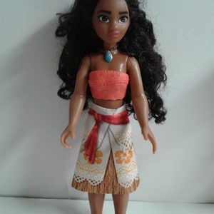 May include: A brown-skinned doll with long black curly hair wearing a coral-colored halter top, a white and brown skirt with floral designs, and a blue necklace.