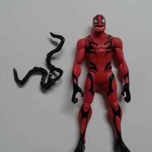 Pode incluir: Figura de a&ccedil;&atilde;o vermelha e preta de um super-her&oacute;i com um acess&oacute;rio de tent&aacute;culo preto.