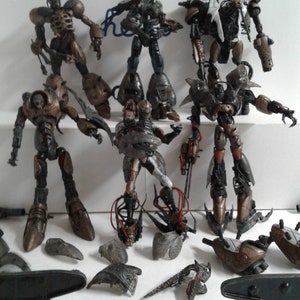 Può includere: Una collezione di sette action figure in plastica di colore grigio scuro e marrone con varie armi e accessori. Le figure sono in una varietà di pose dinamiche. Alcune delle figure mancano di parti, come braccia, gambe e armi.