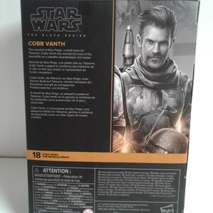 May include: A Star Wars: The Black Series action figure of Cobb Vanth, the Marshal of Mos Pelgo, from the Mandalorian TV series. The figure is posed with a blaster rifle in his right hand and a determined expression on his face. The packaging features a black and gold background with the Star Wars logo and the character's name.