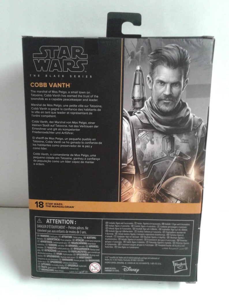 May include: A Star Wars: The Black Series action figure of Cobb Vanth, the Marshal of Mos Pelgo, from the Mandalorian TV series. The figure is posed with a blaster rifle in his right hand and a determined expression on his face. The packaging features a black and gold background with the Star Wars logo and the character's name.