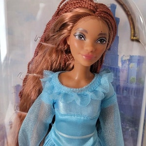 May include: A doll with long brown braided hair wearing a light blue dress with a ruffled neckline.