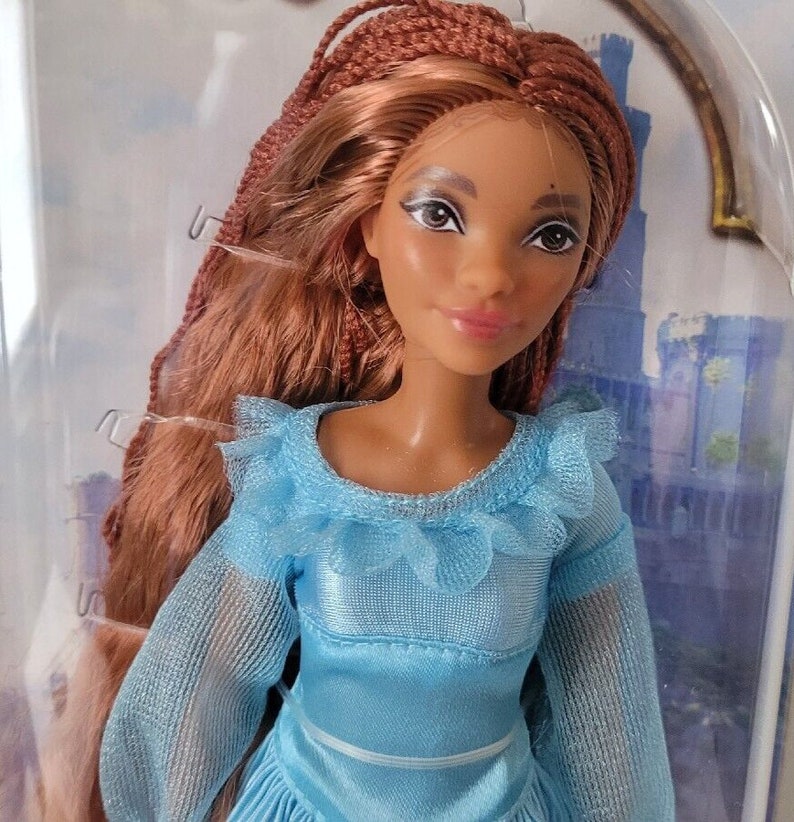 May include: A doll with long brown braided hair wearing a light blue dress with a ruffled neckline.