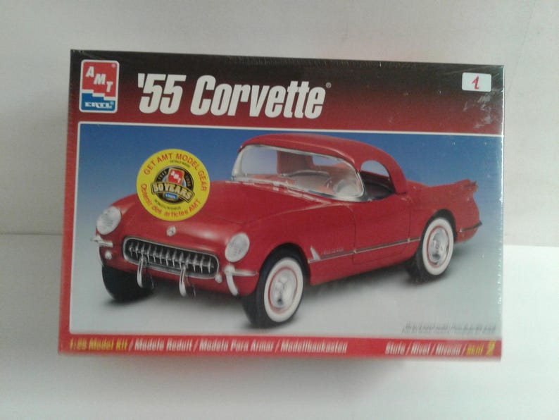 Pu&ograve; includere: Scatola di un modellino di una Corvette '55 rossa. La scatola presenta la scritta "'55 Corvette" e il marchio "AMT". Il modello di auto &egrave; rosso con pneumatici a fascia bianca. Un adesivo giallo recita "50 Years".
