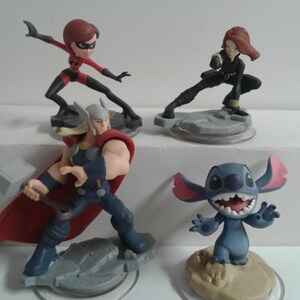 May include: Four Disney character figurines: a red and black superheroine, a blue and red superhero, a black and red superheroine, and a blue alien with large ears. The figurines are on circular bases.