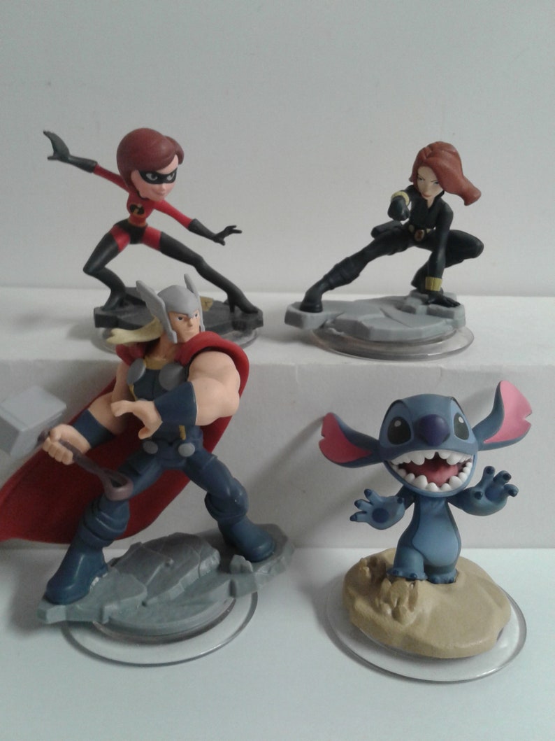 May include: Four Disney character figurines: a red and black superheroine, a blue and red superhero, a black and red superheroine, and a blue alien with large ears. The figurines are on circular bases.
