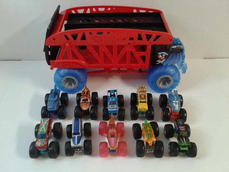 Może przedstawiać: Kolekcja zabawkowych monster truck&oacute;w w r&oacute;żnych kolorach i wzorach. Ciężar&oacute;wki mają duże koła i szczeg&oacute;łową grafikę. Duża czerwona ciężar&oacute;wka z niebieskimi kołami znajduje się na g&oacute;rze. Ciężar&oacute;wki są ułożone na białej powierzchni.