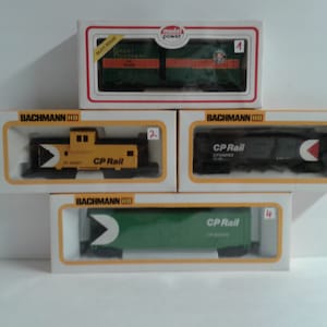 May include: Four model train boxcars in their original packaging. The boxcars are all different colours, including green, yellow, and black. The boxcars are labelled "CP Rail".