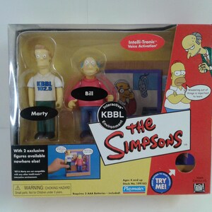 May include: The Simpsons toy playset features two figures, Marty and Bill, from the animated television show. The set includes an interactive KBBL environment and a voice activation feature. The box is red, yellow, and blue with the show's logo and characters.