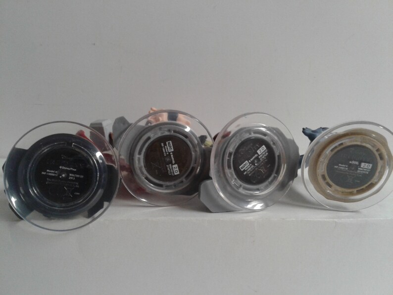 May include: Four small plastic figurines with clear plastic bases. The bases have black labels with white text. The text on the labels reads "Disney", "Marvel", "Star Wars", and "Pixar".