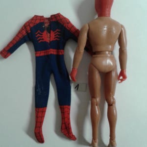 Op de afbeelding: Een vintage Spider-Man-actionfiguur met een rood en blauw pak en een rood masker. De figuur mist zijn hoofd en handen, maar het lichaam is intact. De figuur staat met zijn benen licht uit elkaar. De figuur staat op een witte achtergrond.