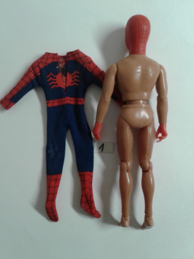 Op de afbeelding: Een vintage Spider-Man-actionfiguur met een rood en blauw pak en een rood masker. De figuur mist zijn hoofd en handen, maar het lichaam is intact. De figuur staat met zijn benen licht uit elkaar. De figuur staat op een witte achtergrond.